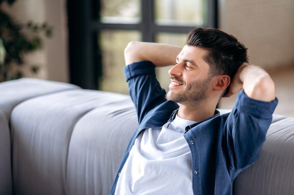 A happy young man sitting on the sofa with both hands on his head, looking very relieved