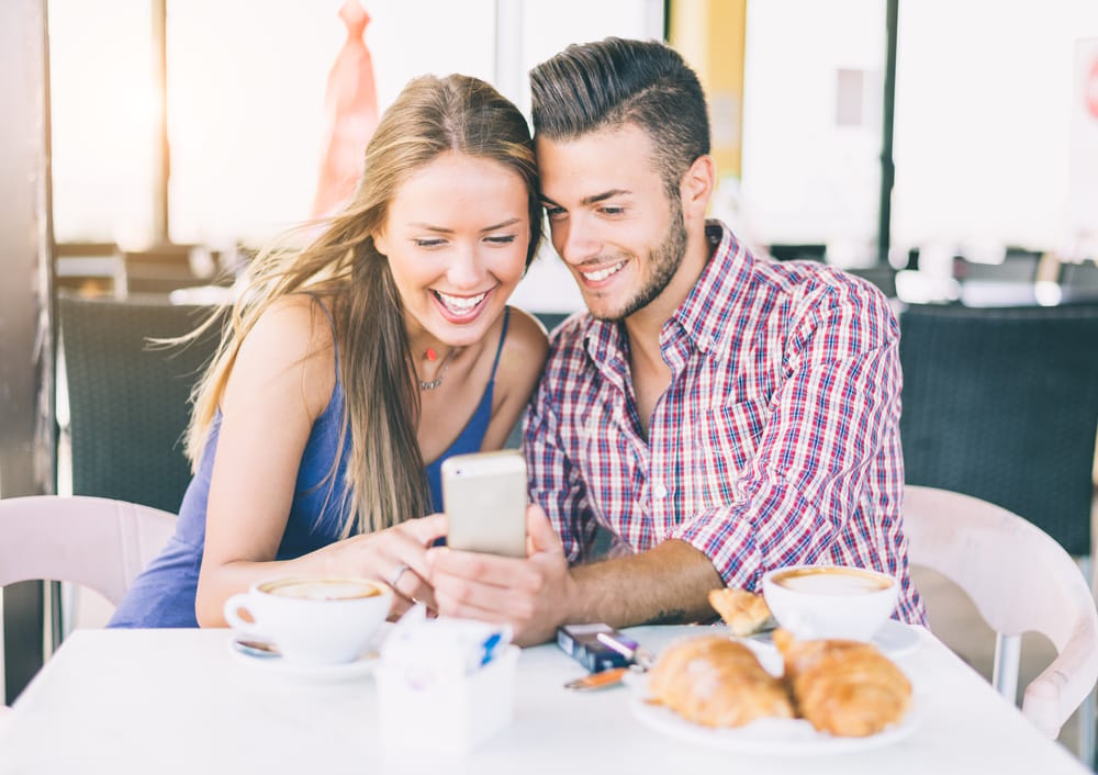 A happy couple in a coffee shop looking at pictures in a phone