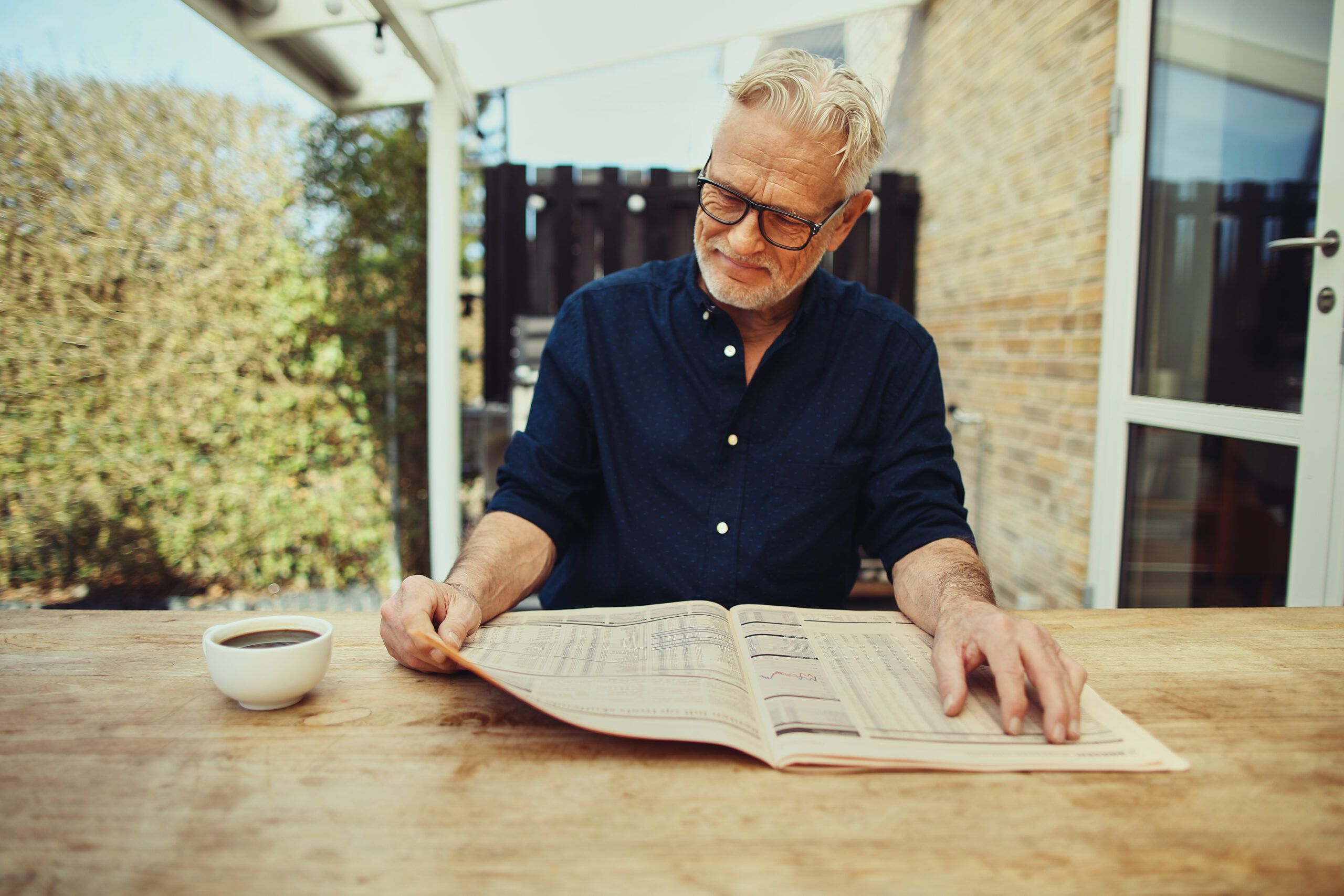 A retired senior man having coffee while reading the paper.