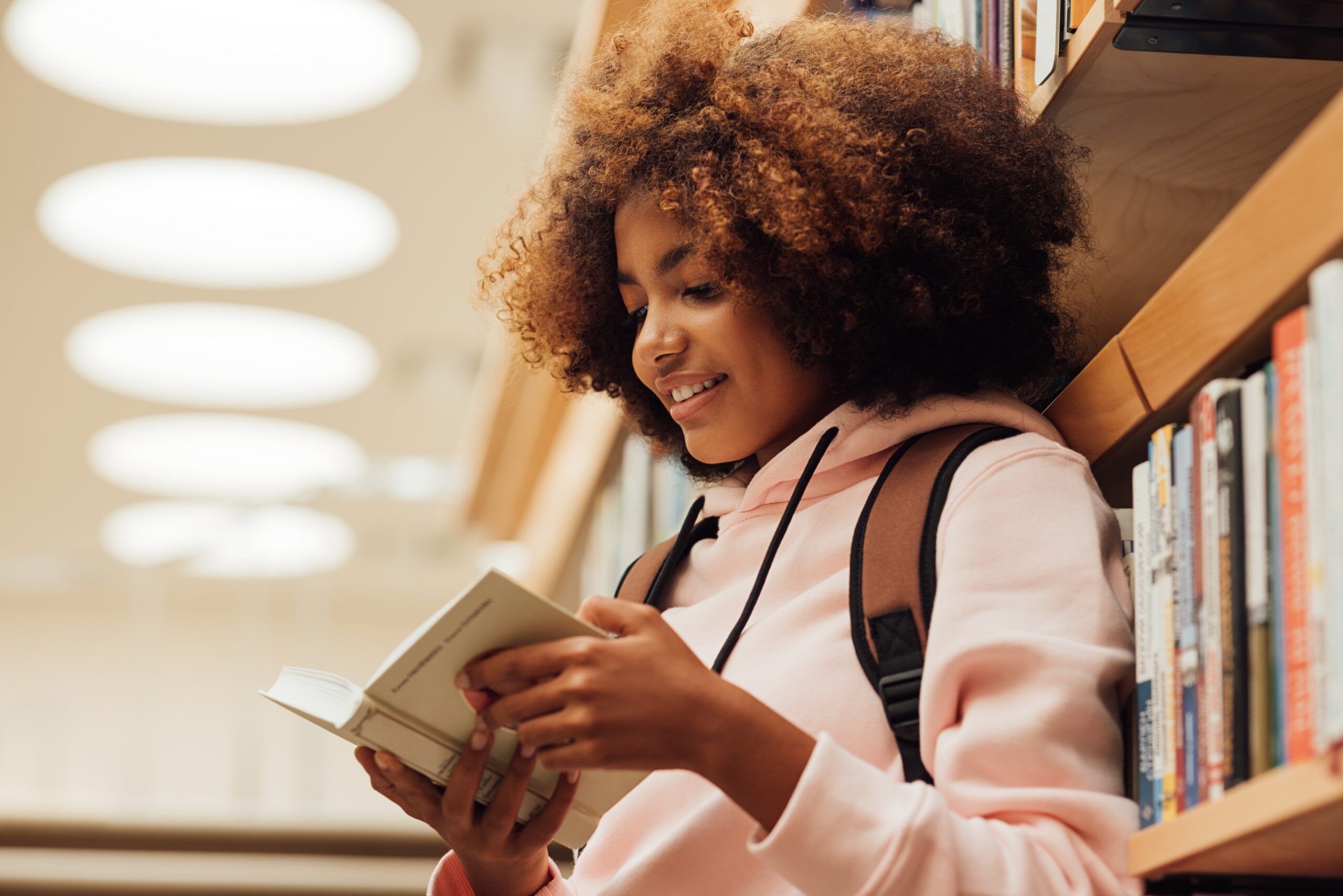 Girl with her backpack reading a book in the library.