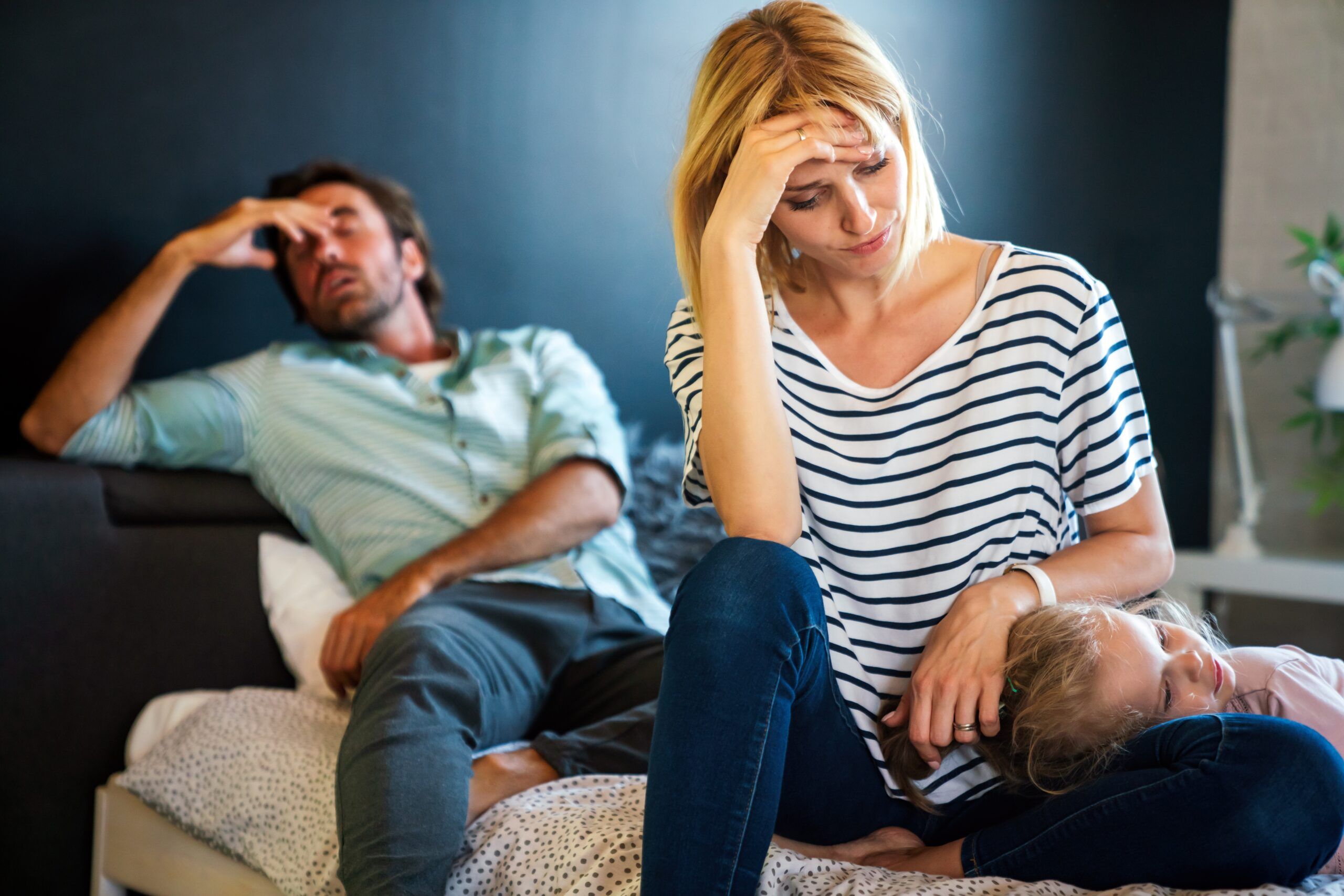 An exhausted mother and father sitting on the couch with their young child.