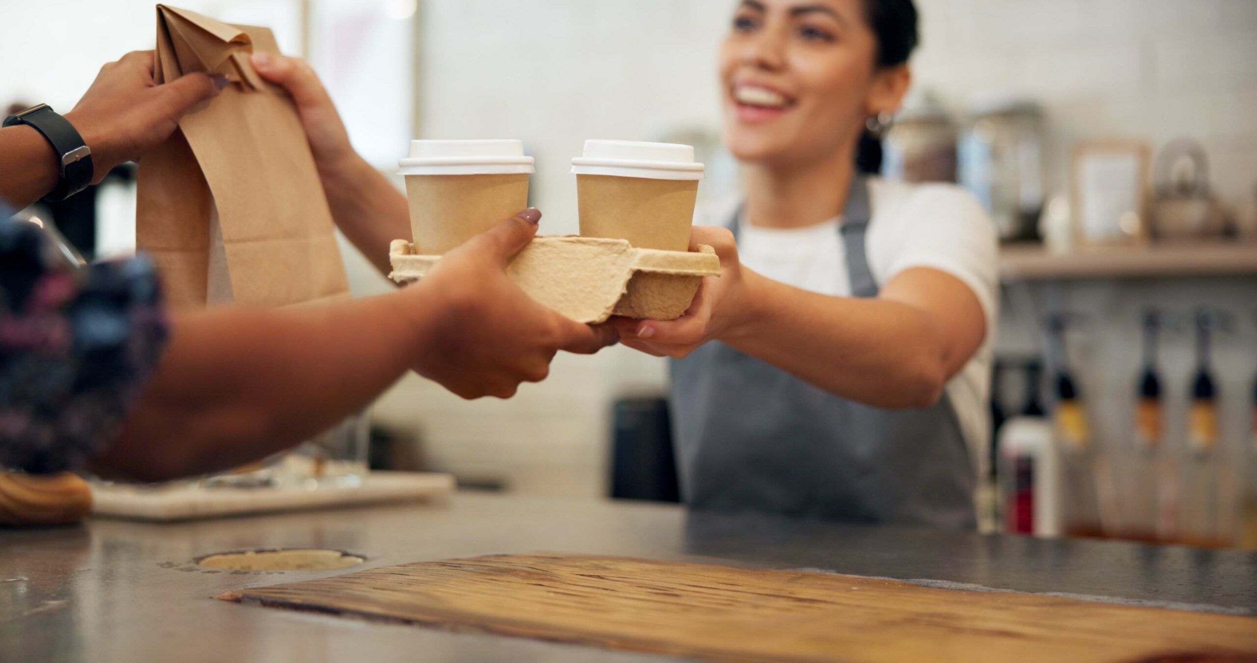 A coffee shop barista handing an order to her customer.