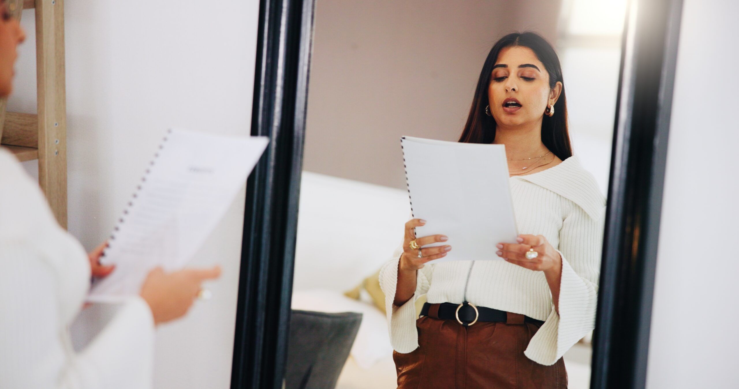 Nervous young woman rehearsing speech in front of a mirror.