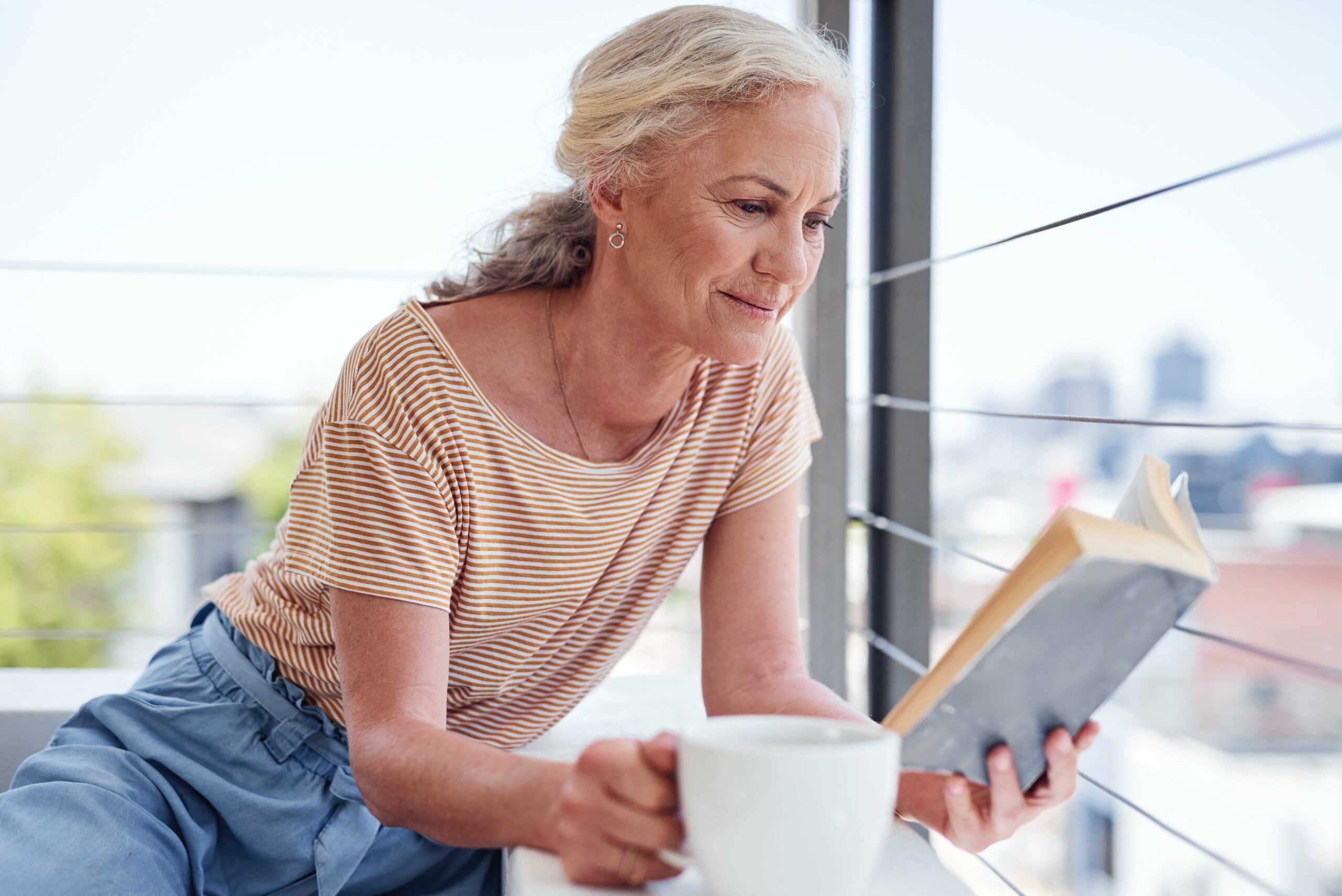A senior woman reading a book and relaxing with coffee.