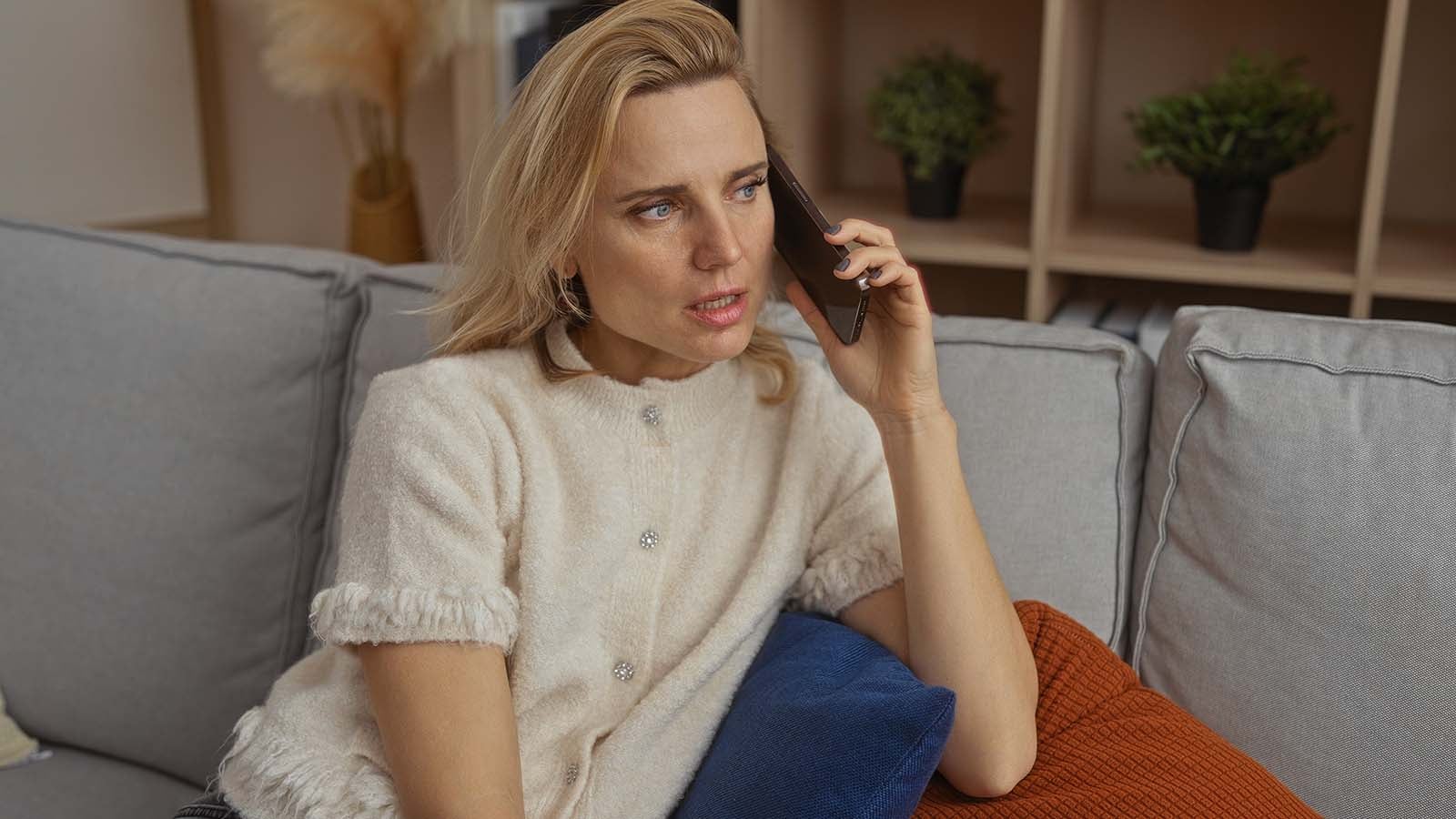 Woman talking on phone in cozy living room with beige sweater and blonde hair,