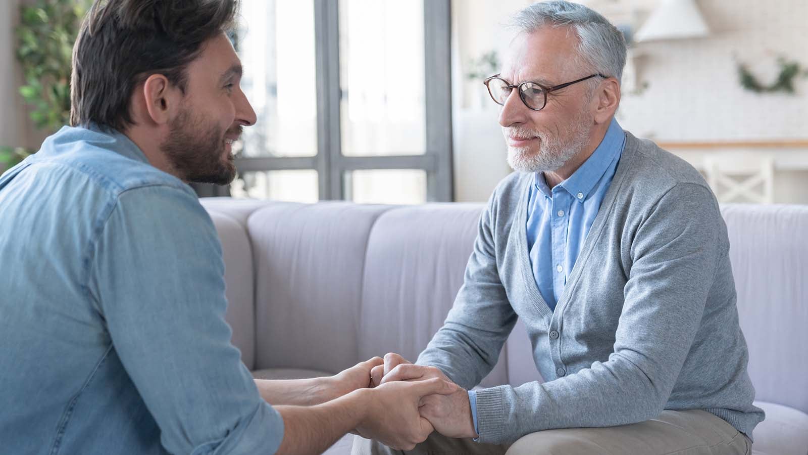 Young adult caucasian son listening and supporting his old elderly senior father at home indoors.