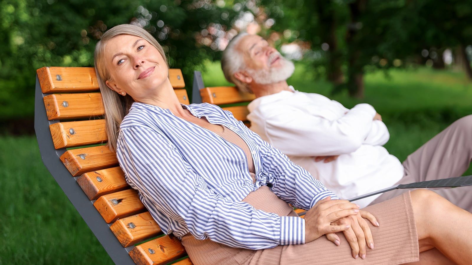 Lovely senior couple resting on wooden sunbeds in park