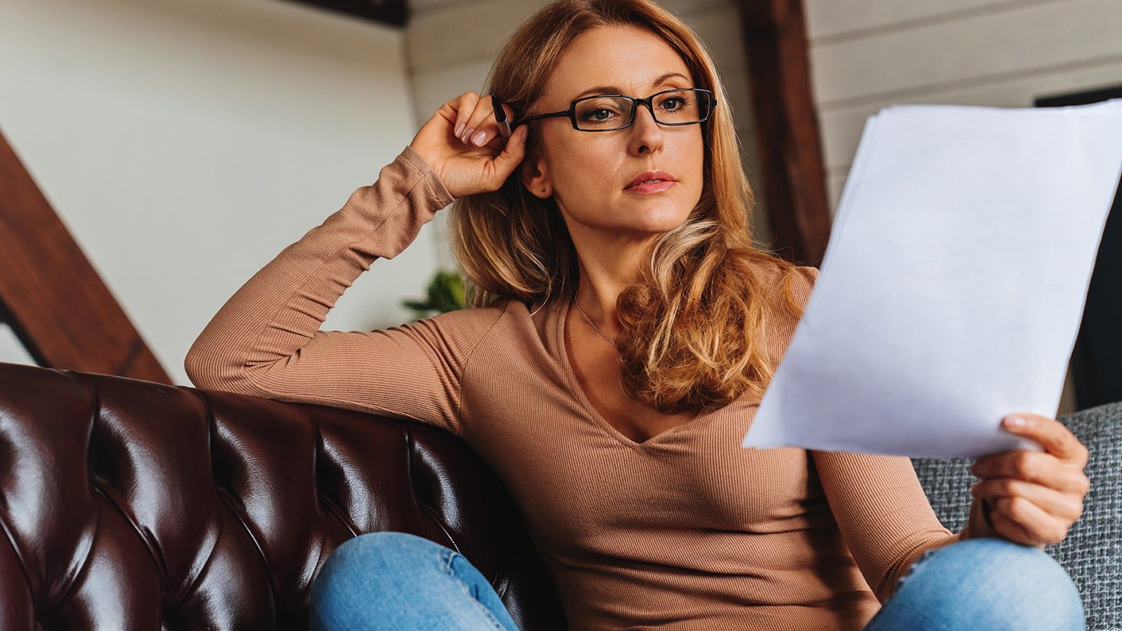 Confident woman sitting on couch reaching documents