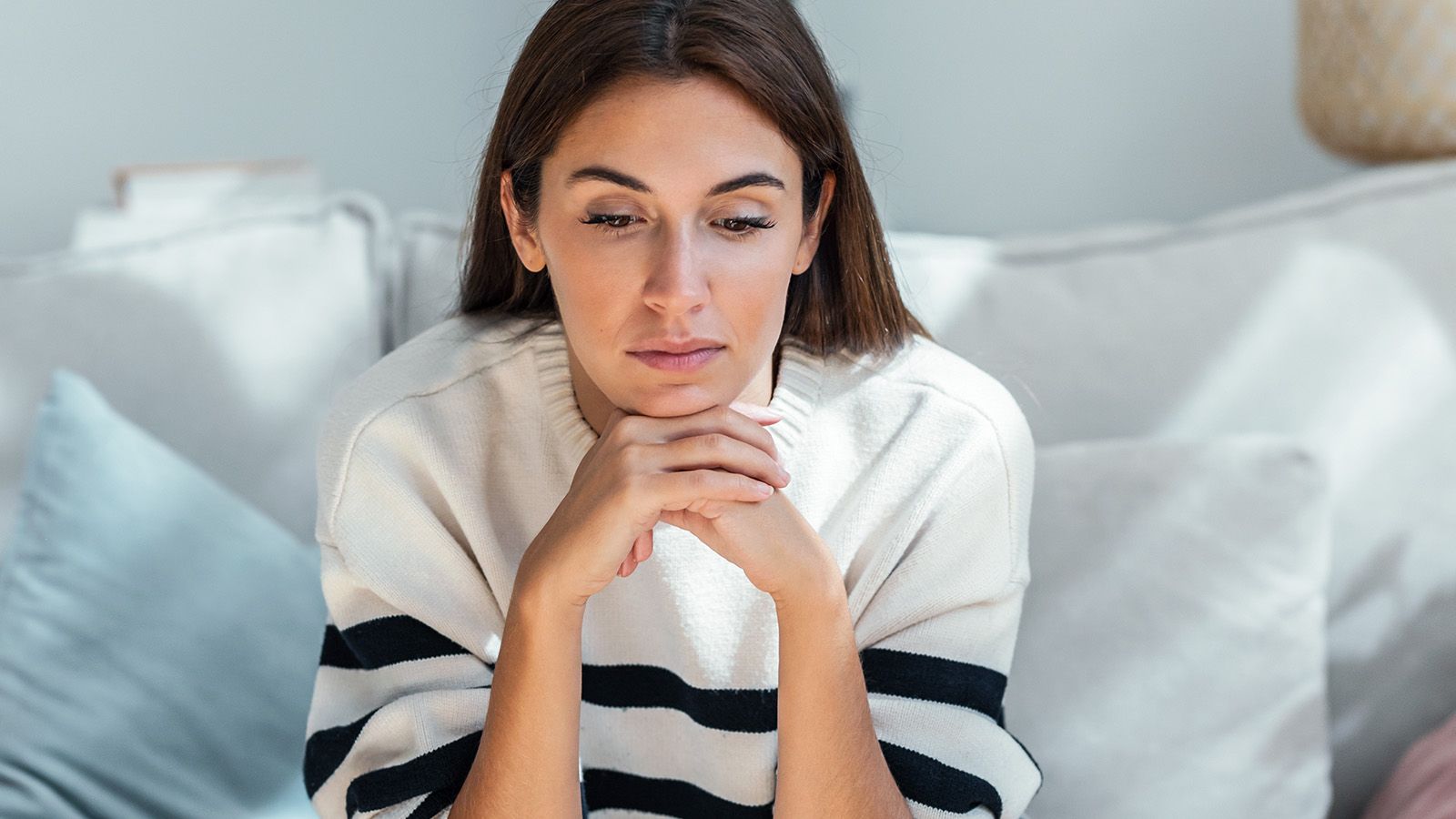 Shot of depressed young woman thinking about her problems while sitting on the sofa at home.