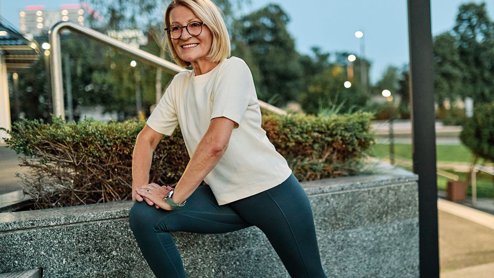 Portrait of a middle aged mature beautiful sport woman smiling happy and confident. Standing and doing exercise and stretching in city park outdoors