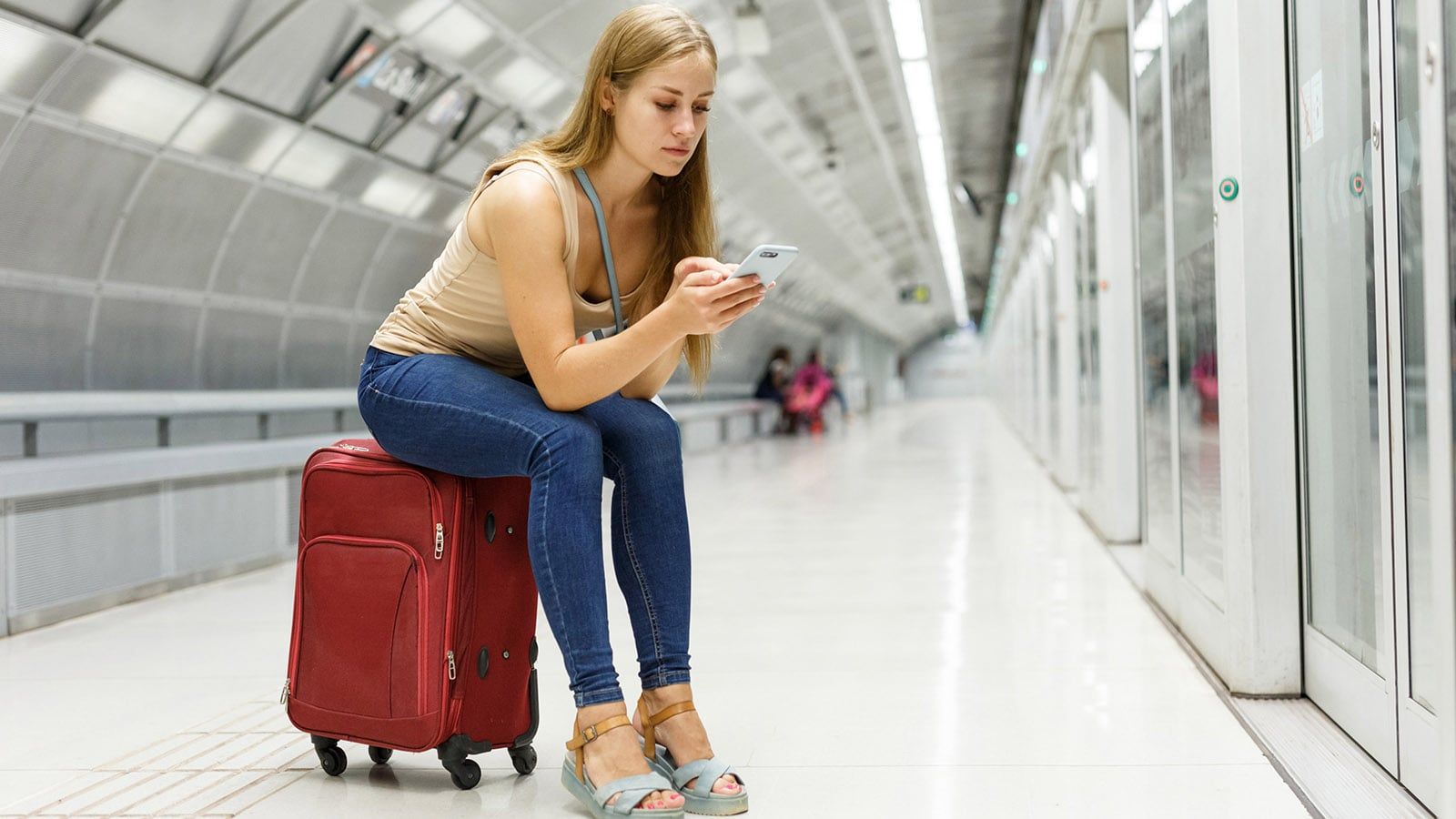 Young woman waiting at the airport sitting on her luggage bored and early for a flight