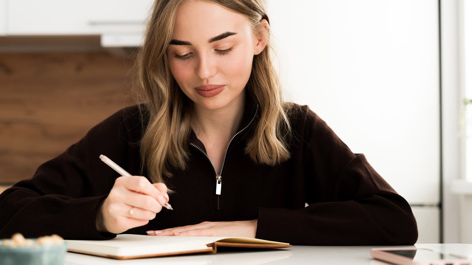 Focused young woman writing notes in notebook thoughtful and concentrated. studying, journaling at home