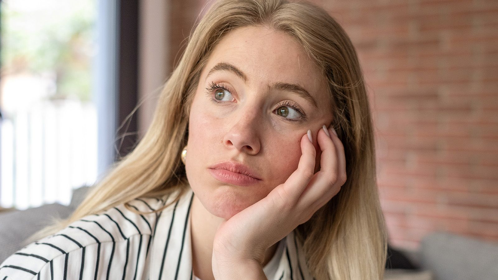 A pensive young woman sits in a cozy living