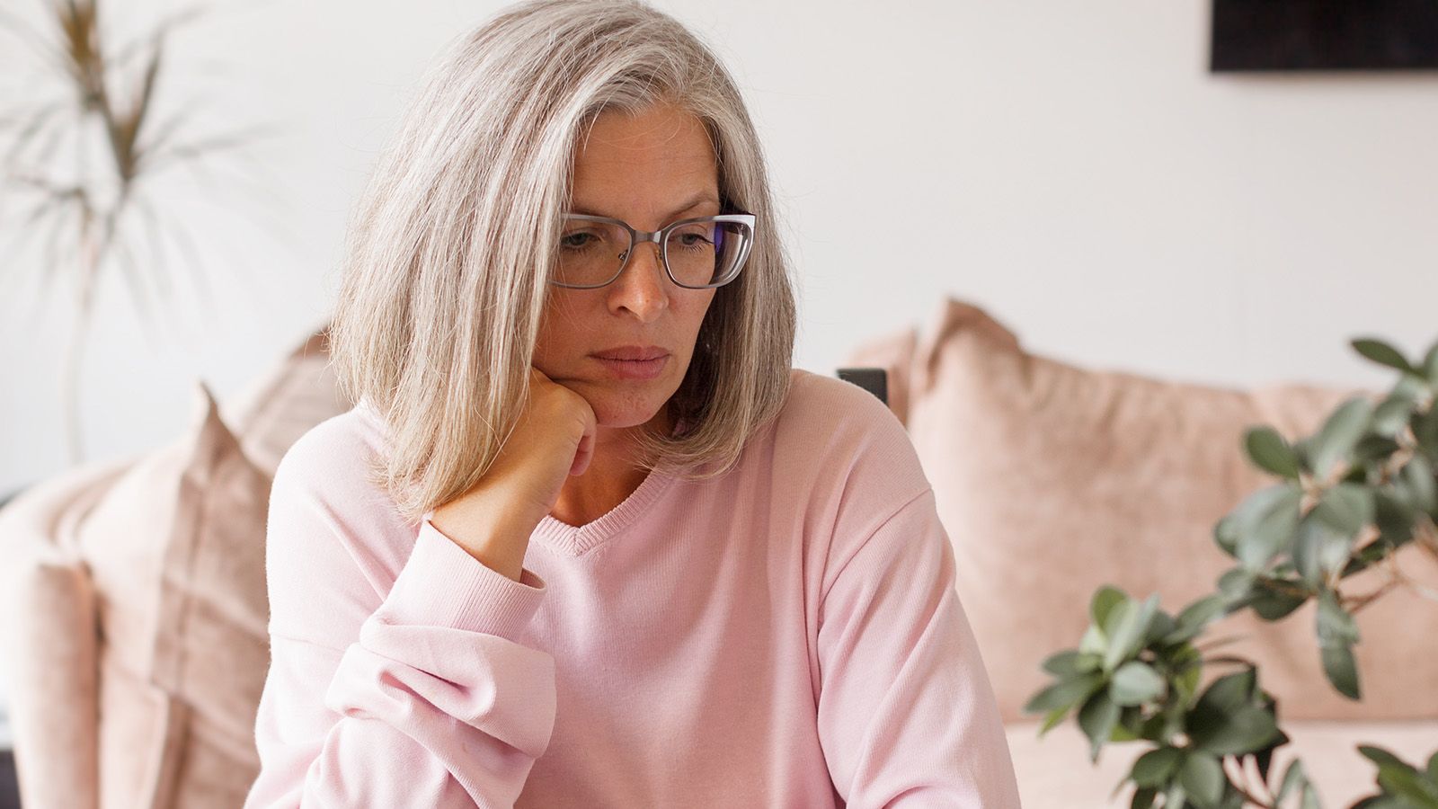 Thoughtful mature woman lost in thoughts, memories, sitting on couch at home alone, upset pensive middle aged female thinking about problems, pondering Sad middle aged female in living room