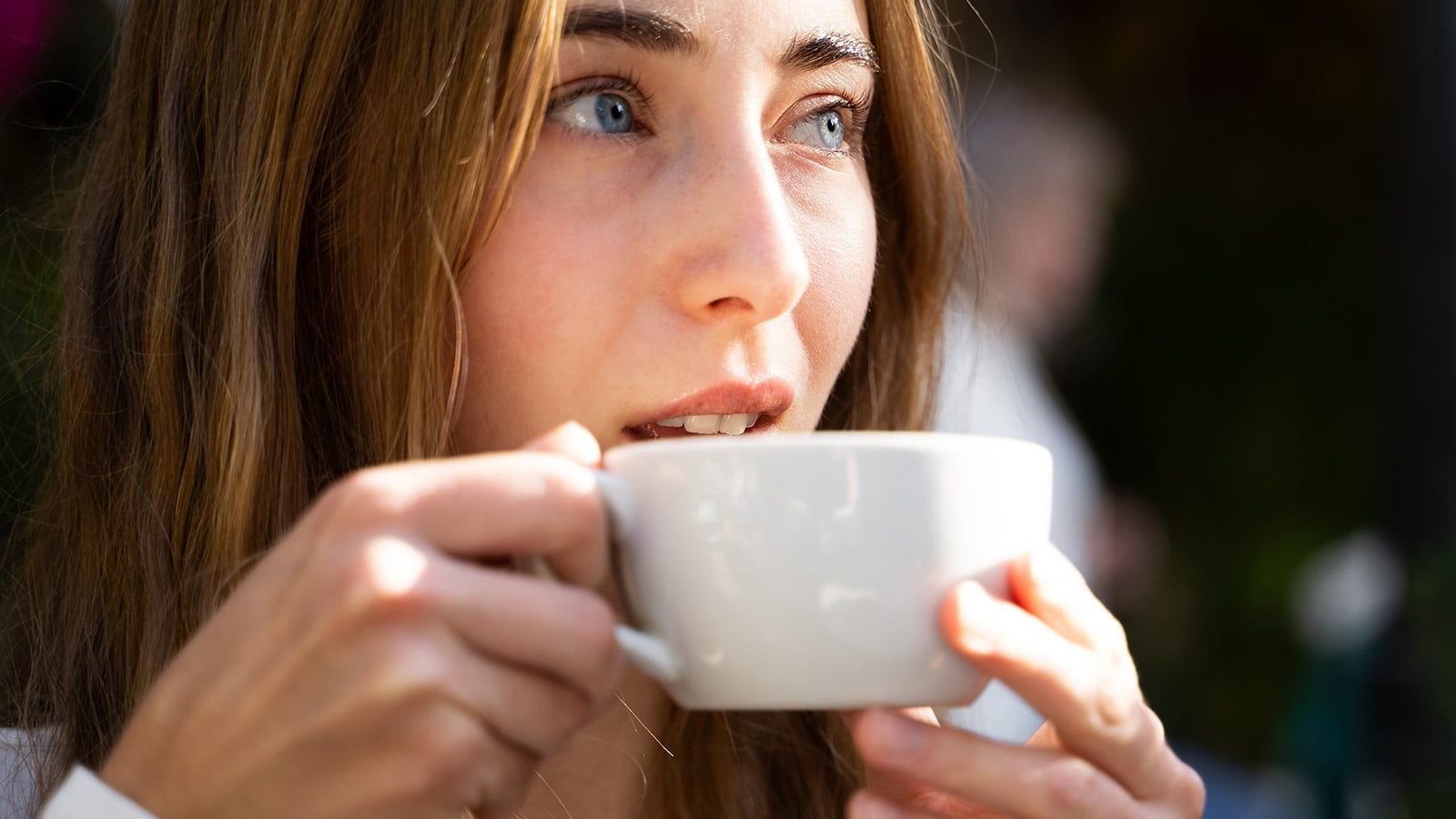 Young woman drinking coffee outdoors at cafe, enjoying warm drink and looking away, relaxed lifestyle, leisure moment
