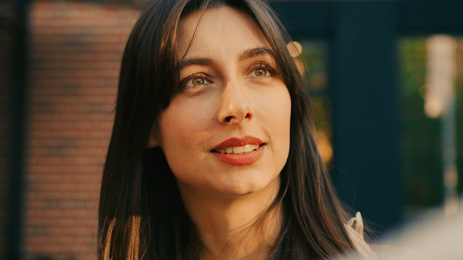 Portrait of pretty Caucasian woman talking with someone at street. Sunlight shining bright directly on face. People actively communicating with each other. During conversation girl nodding her head.