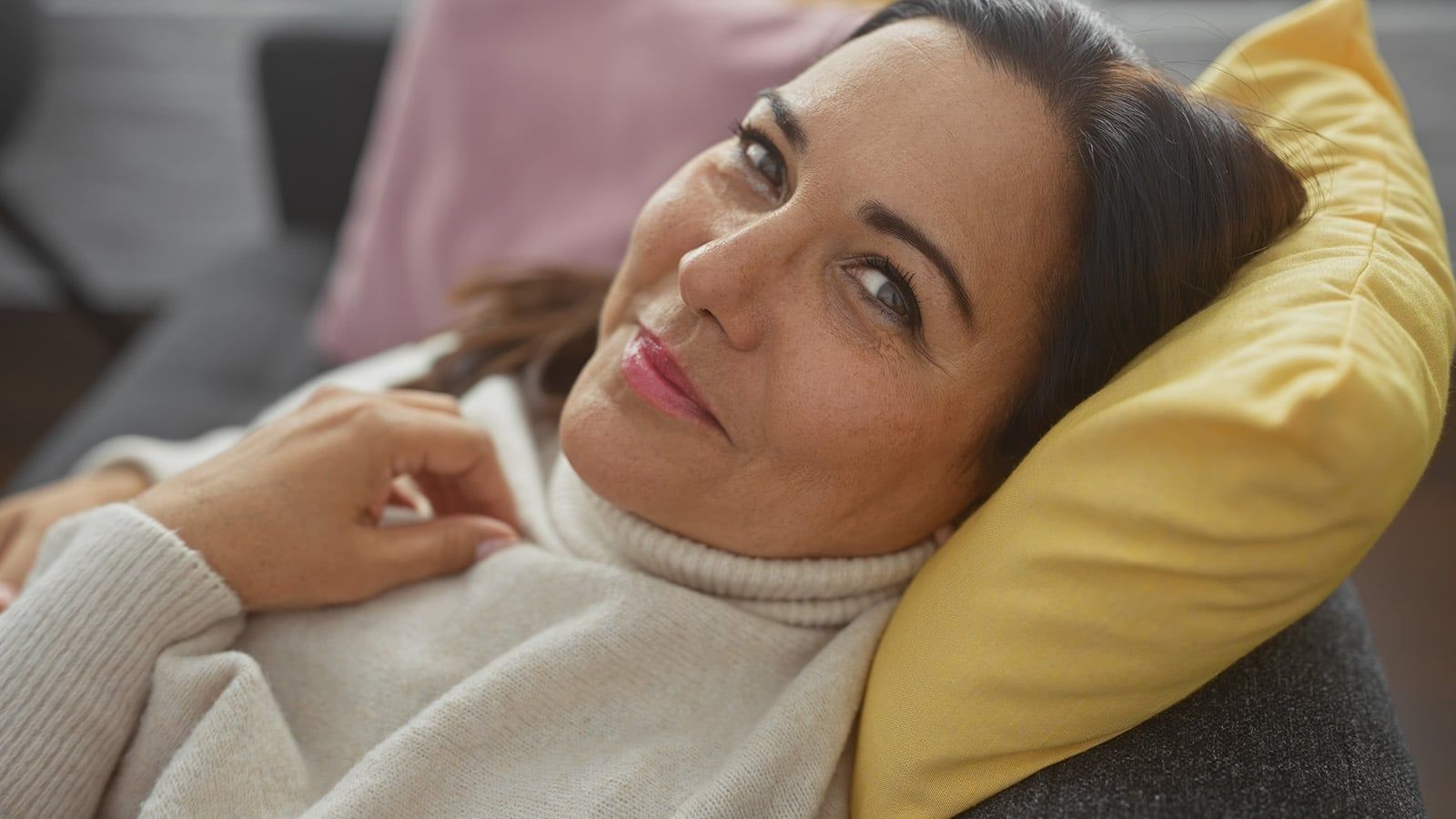 Smiling middle-aged woman relaxing on a couch at home, exuding warmth and comfort.