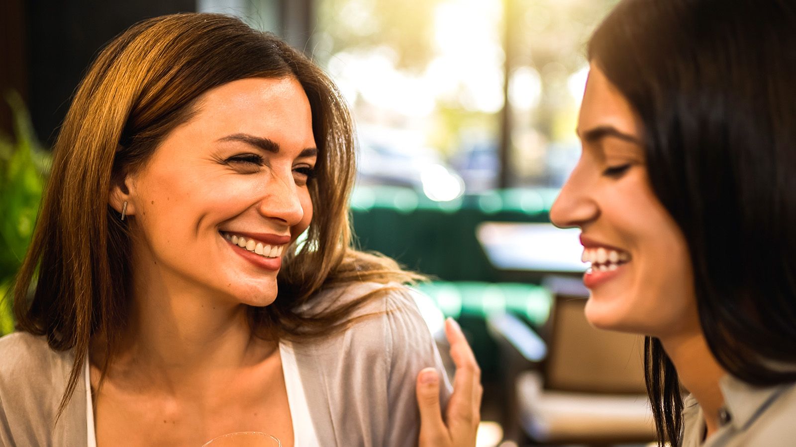 Two girl friends met at the coffee shop to hang out, gossip and talk to each other. They are drinking coffee and orange juice.