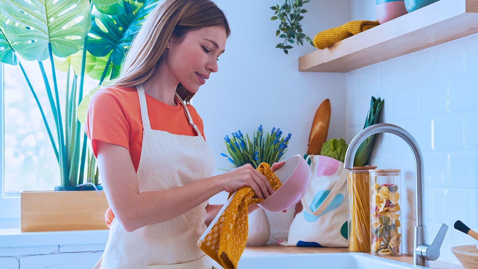 Beautiful young woman dries dishes at the domestic kitchen