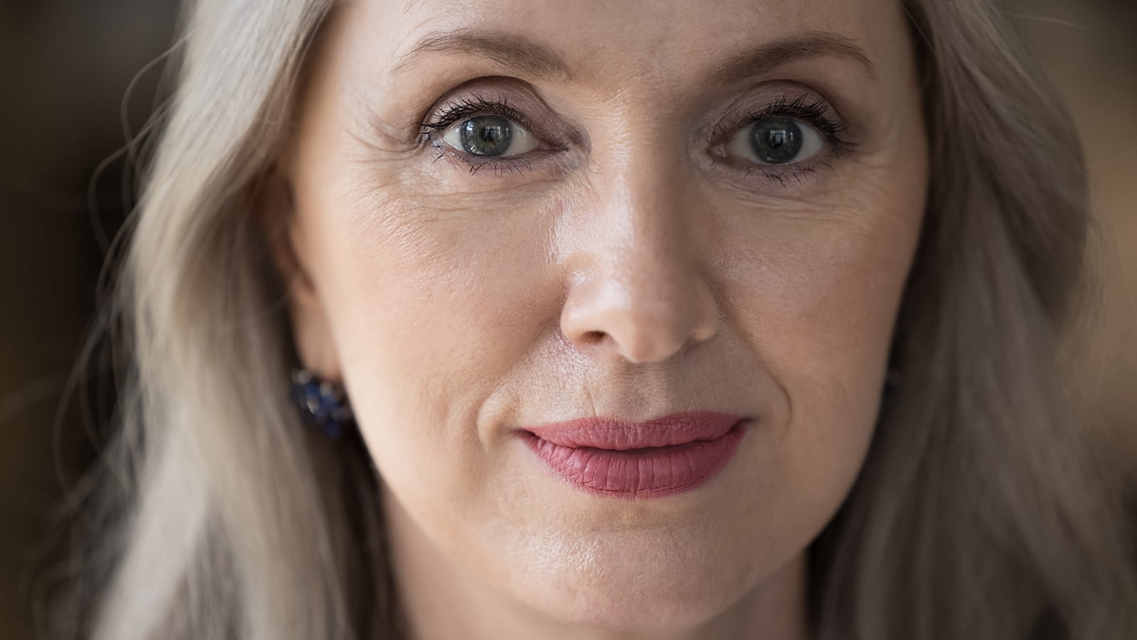 Positive confident beautiful mature woman head shot close up portrait. Pretty grey haired retired lady, middle aged model with makeup looking at camera, posing indoors.