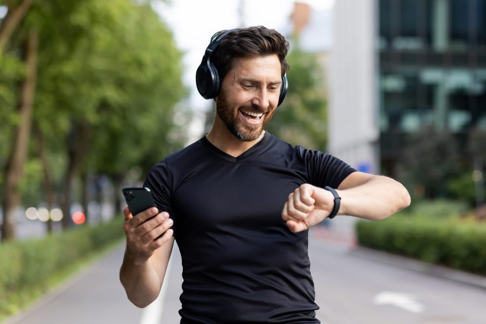 A happy middle age man going on a fitness walk checking his watch, with headphones on his head