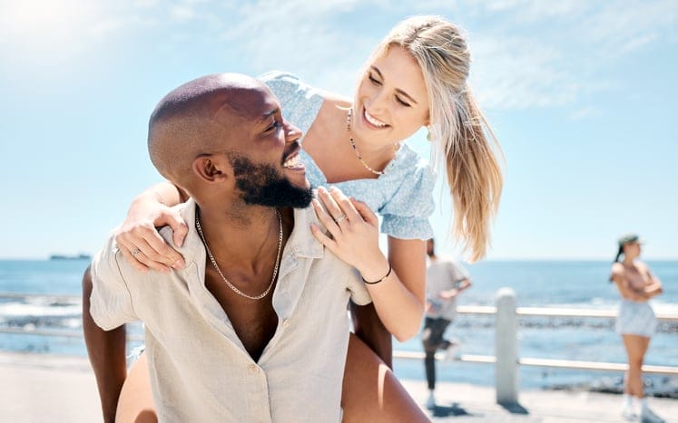 woman riding piggyback on boyfriend at beach
