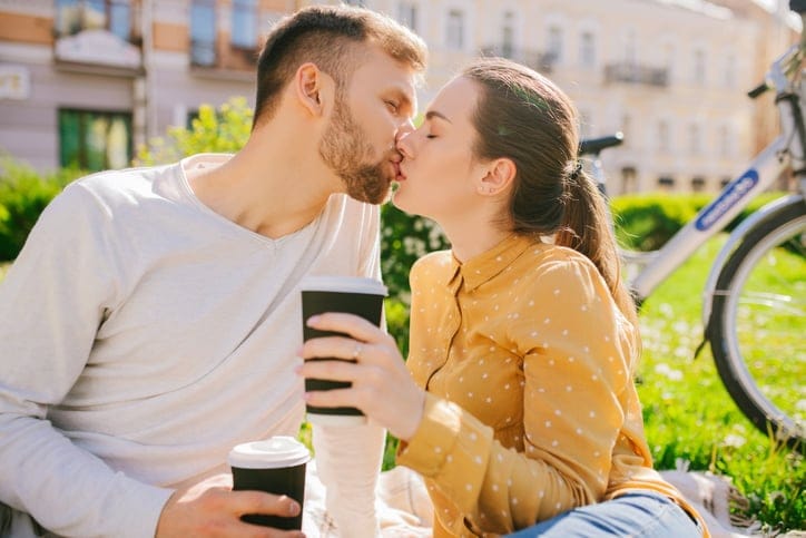 couple with coffee kissing in park