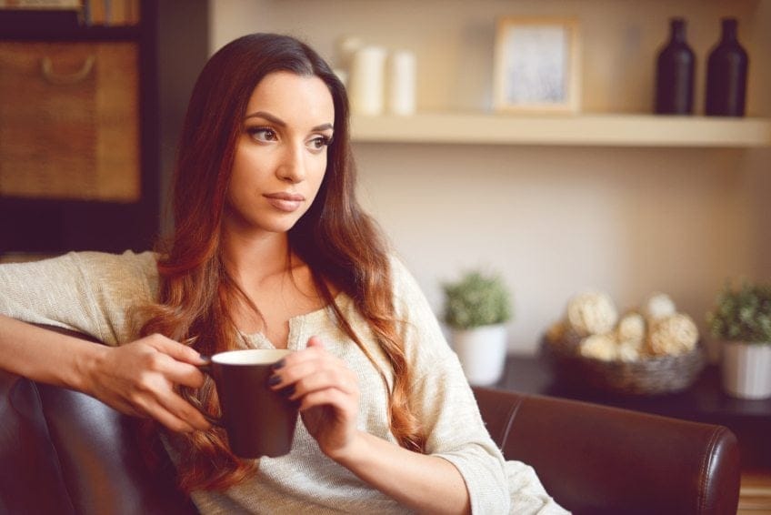 pensive woman drinking tea on couch