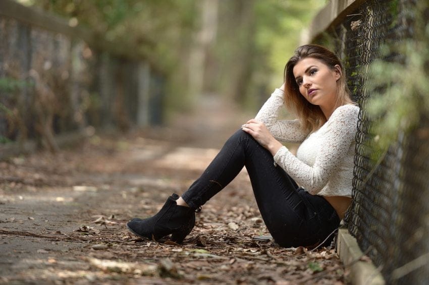 sad woman sitting against fence outside