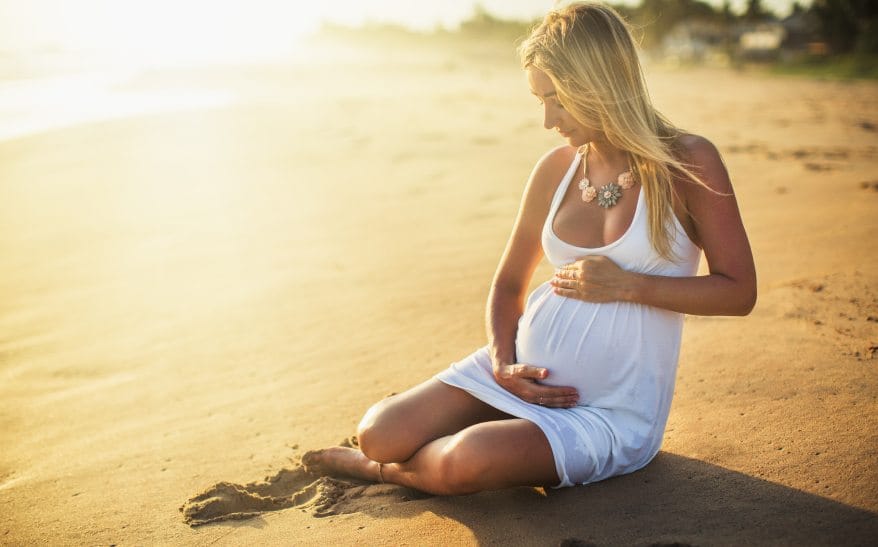 pregnant woman cradling bump on beach