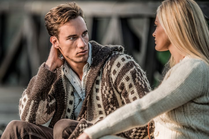 Young fashionable couple sitting on a bridge and talking.
