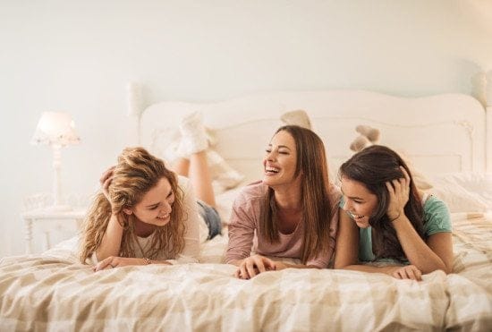 three female friends laughing in bed