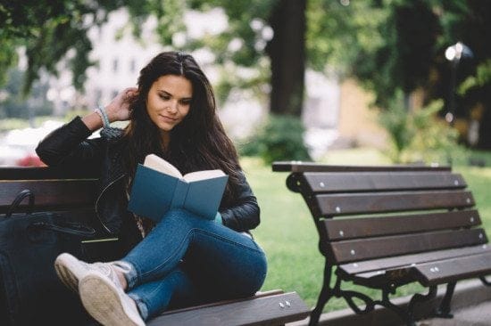 woman reading book on park bench