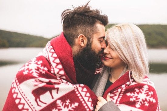 couple cuddling in nordic blanket by lake