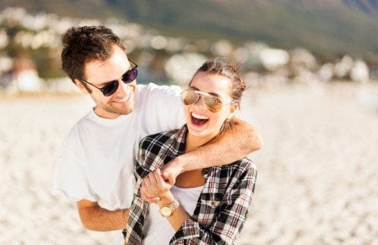 smiling couple in sunglasses on beach