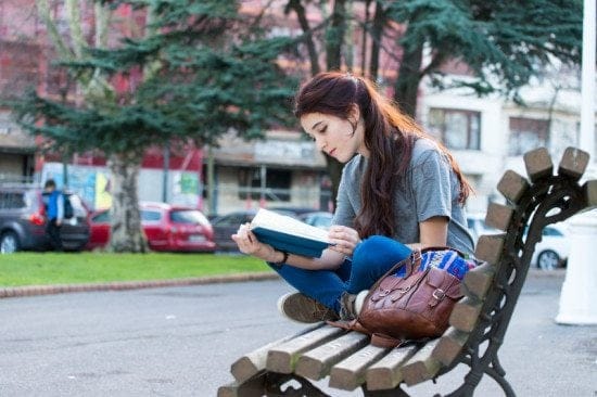 woman reading book on park bench