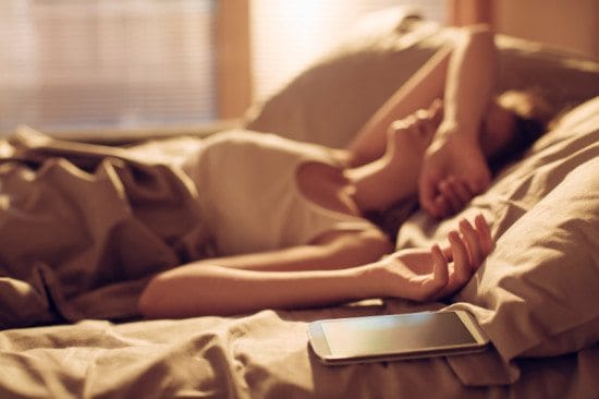 tired woman with phone in bed