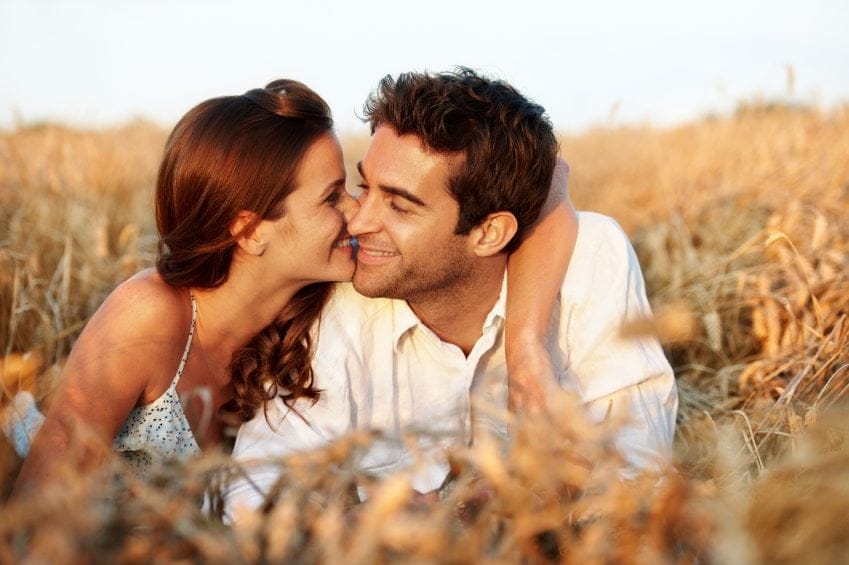 woman kissing man's cheek in field