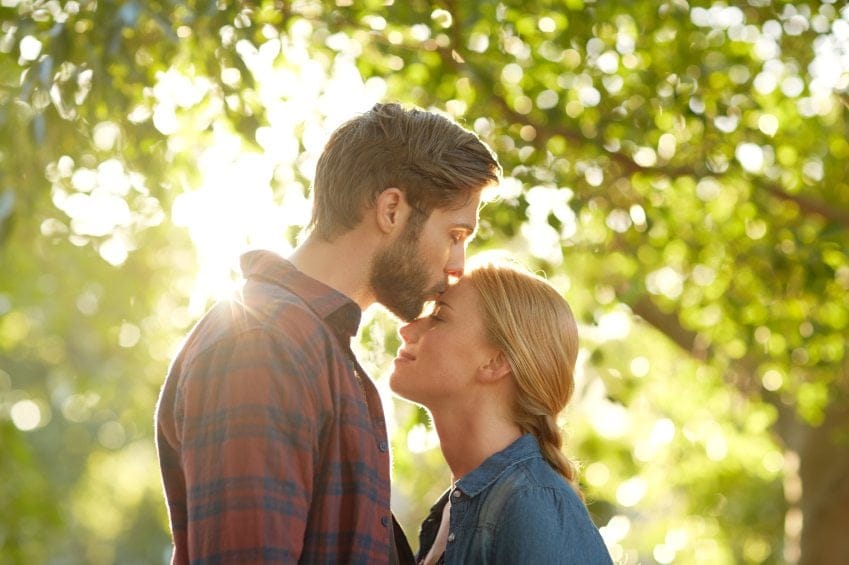 man kissing woman's head romantic sun trees