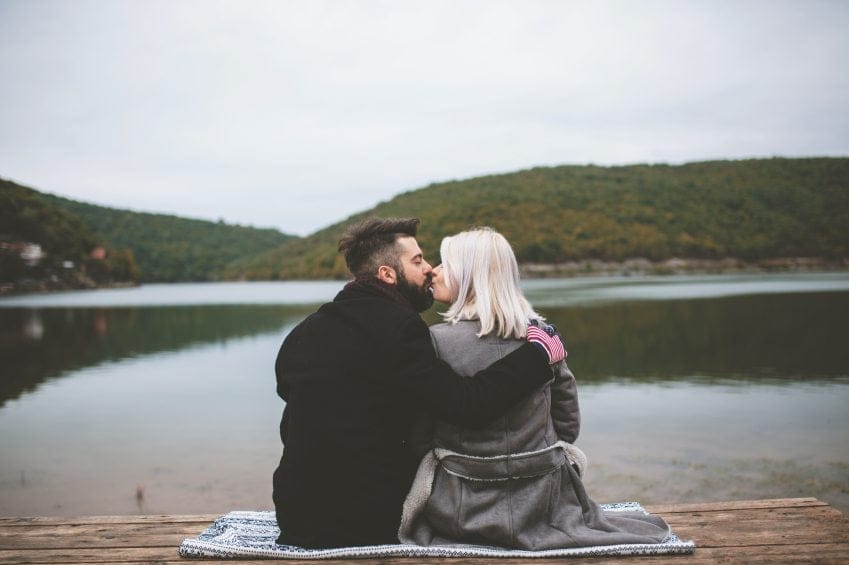 couple kissing during lakeside picnic