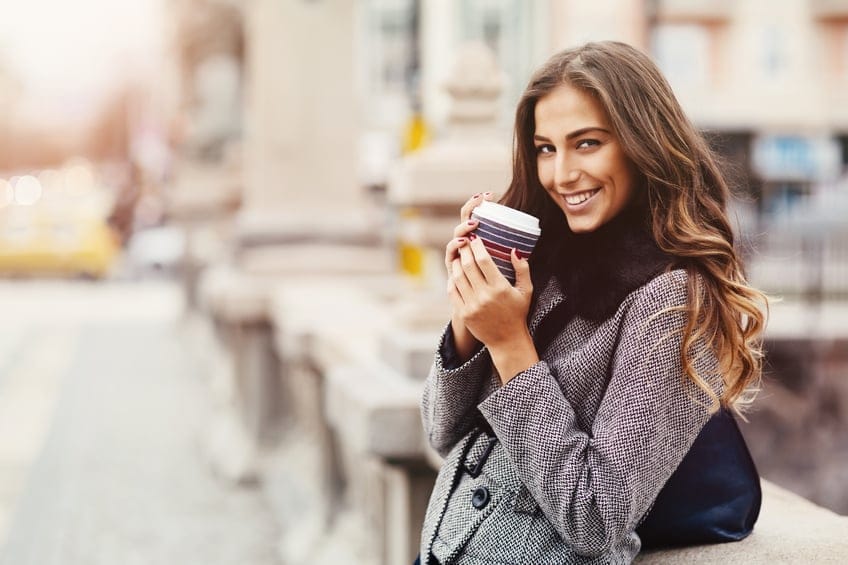 A beautiful girl drinking coffee outside.