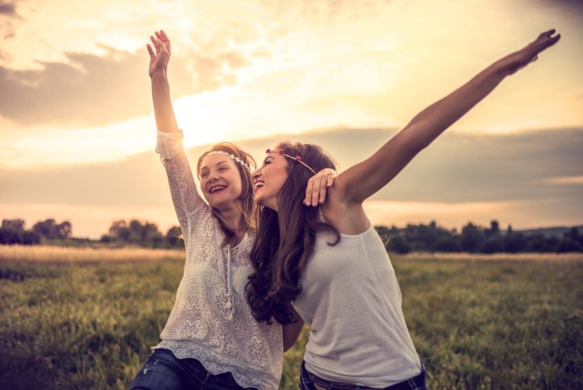 Happy smiley hipsters in field at sunset with open arms.