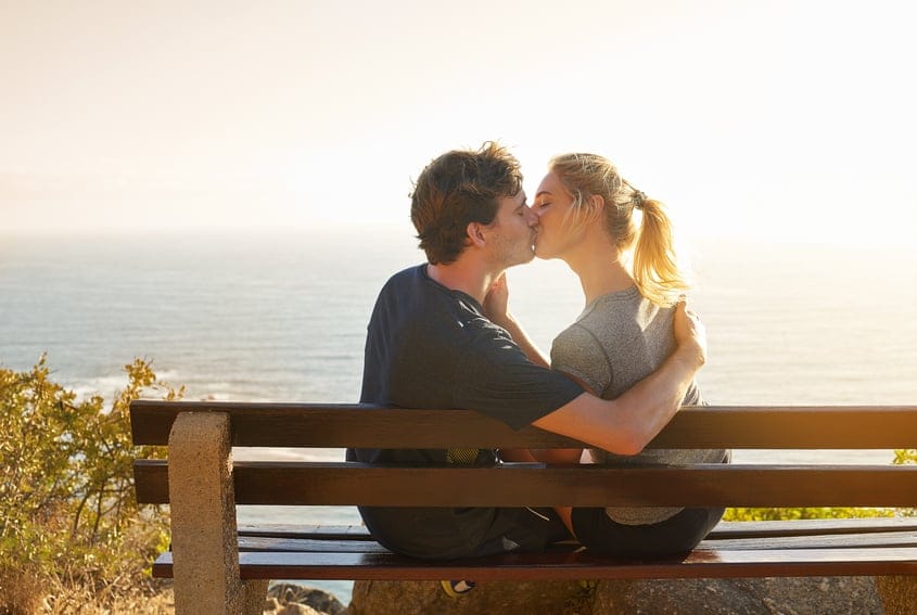 Shot of a loving couple sitting on a bench overlooking the ocean