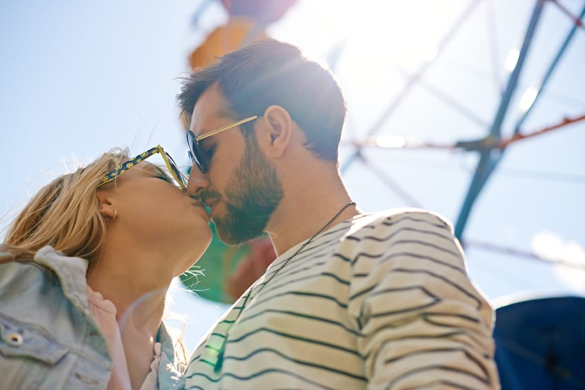 Young couple wearing sunglasses kissing in amusement park