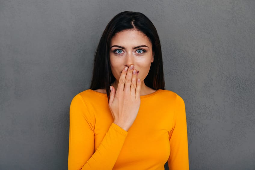 Surprised young woman covering mouth with her hand.