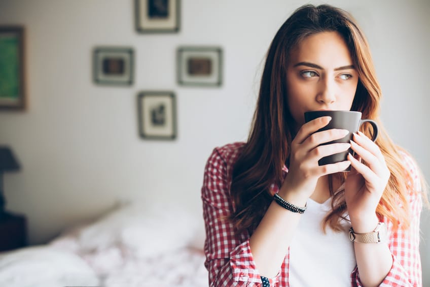 Young woman standing at bedroom and drinking coffee