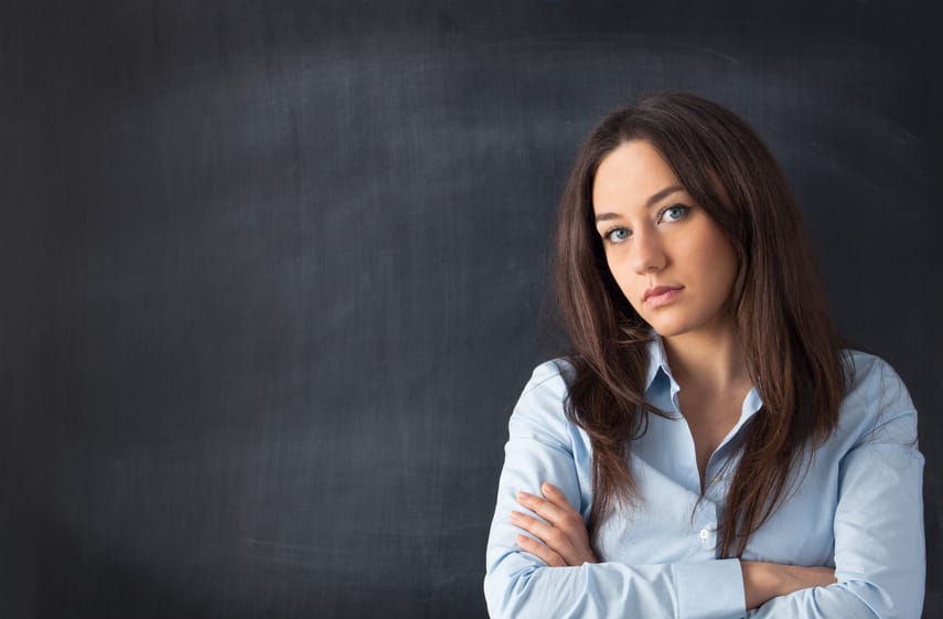 Serious businesswoman standing with arms crossed at blackboard