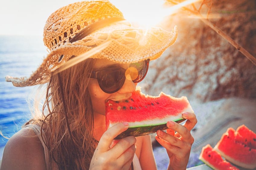 Woman on the beach eating watermelon.