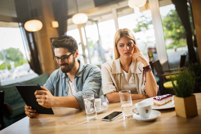 Girlfriend annoyed with boyfriend using digital tablet on date.