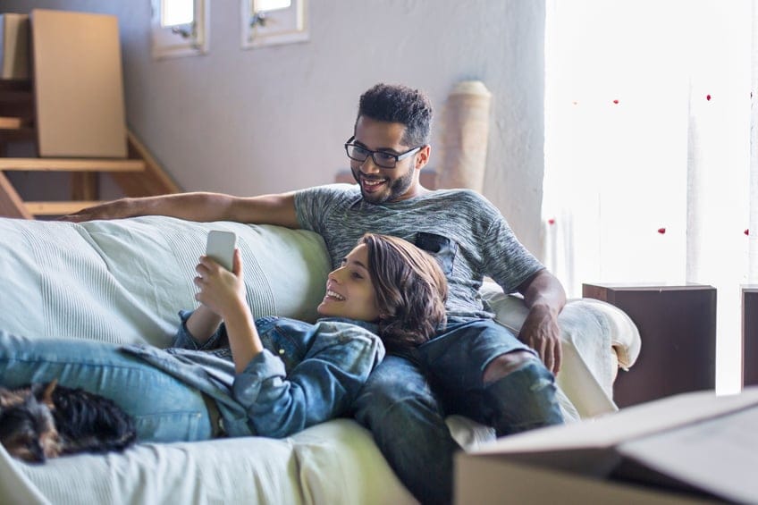 Couple posting on the social network relaxing on the sofa with all the boxes to unpack at the new home.